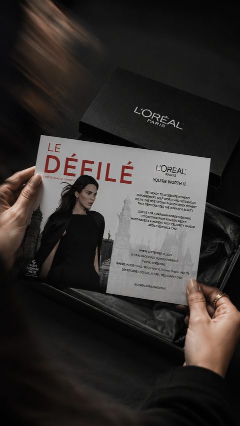 Coffret noir Le Défilé ouvert, avec l’invitation à l’événement tenue en main.