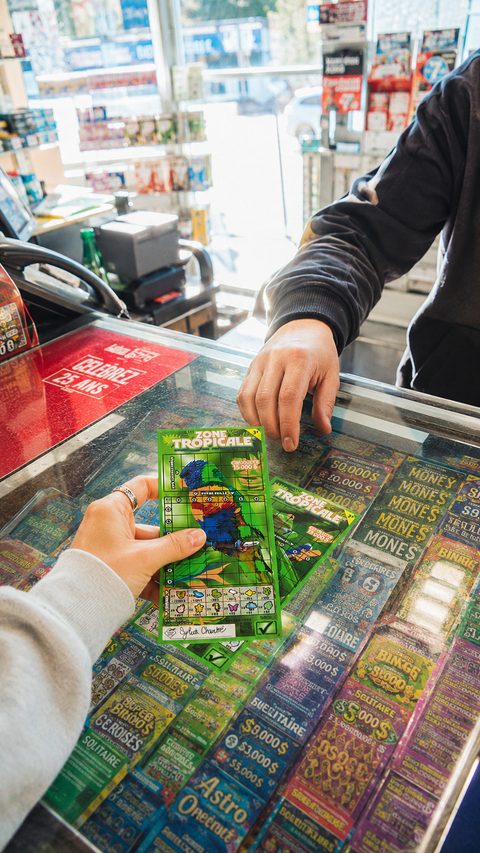 Une cliente prend un billet Zone Tropicale dans le distributeur d’un dépanneur.