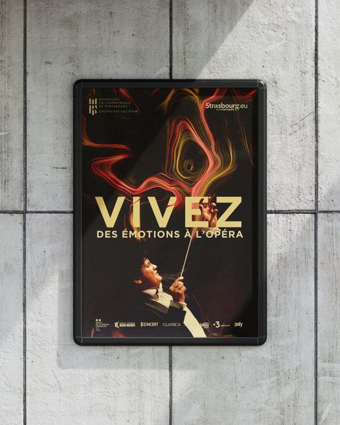 Affiche « Vivez des émotions à l’opéra » dans un cadre noir fixé sur un mur de béton.